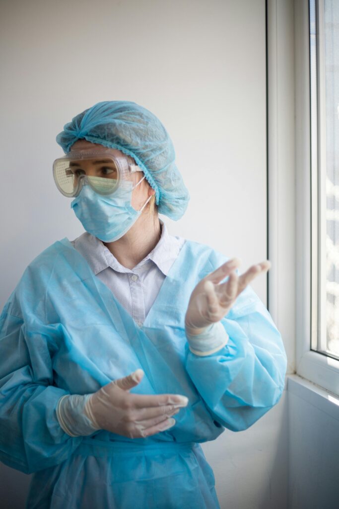 A healthcare professional wearing PPE stands indoors looking out the window.